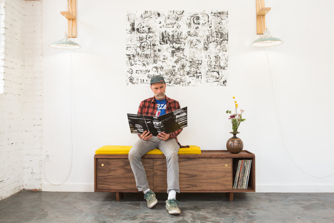 Pete Deeble sitting on a bench cushion, looking at liner notes from an LP