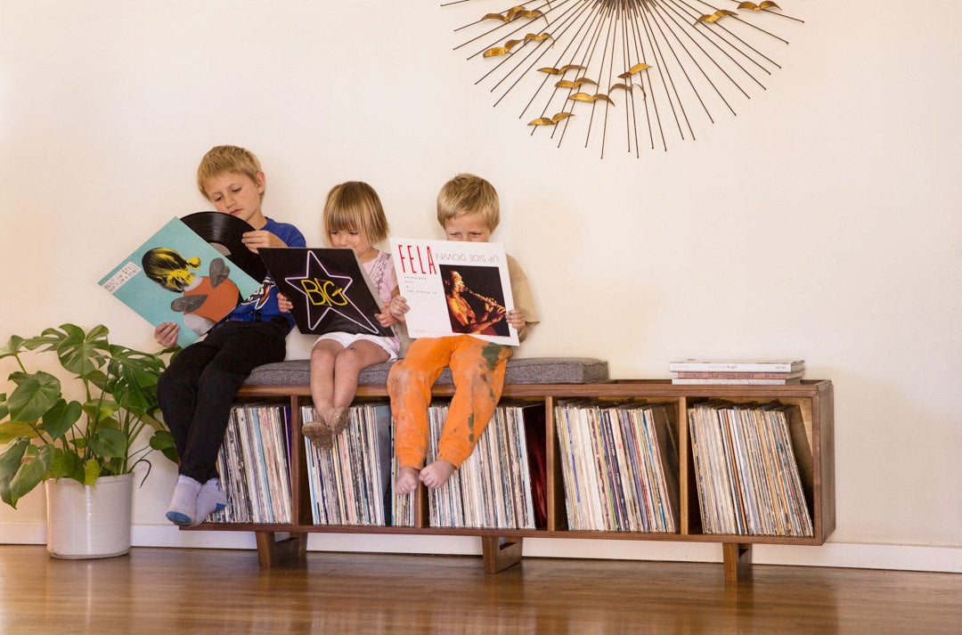 Kids sitting on a vinyl storage bench surrounded by records